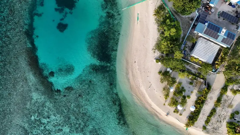 Vue aérienne d'une plage de sable blanc bordée d'une eau turquoise et d'une végétation luxuriante.