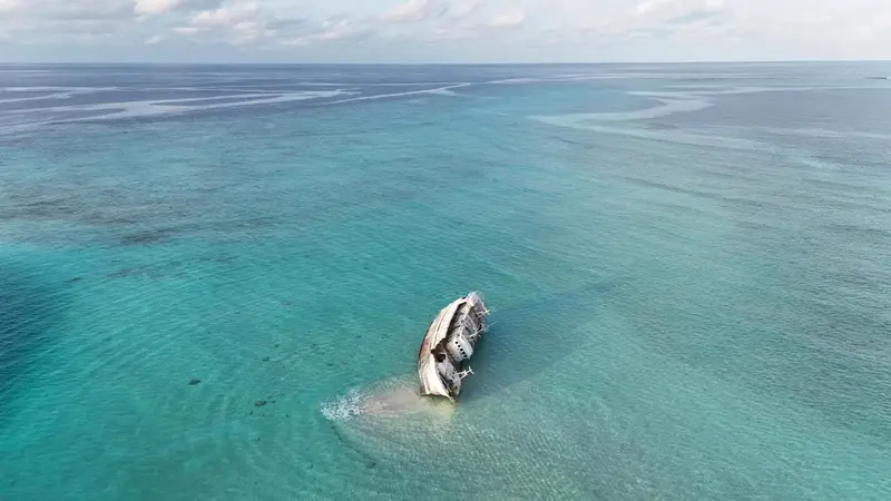 Vue aérienne d'une épave partiellement immergée dans une eau turquoise.