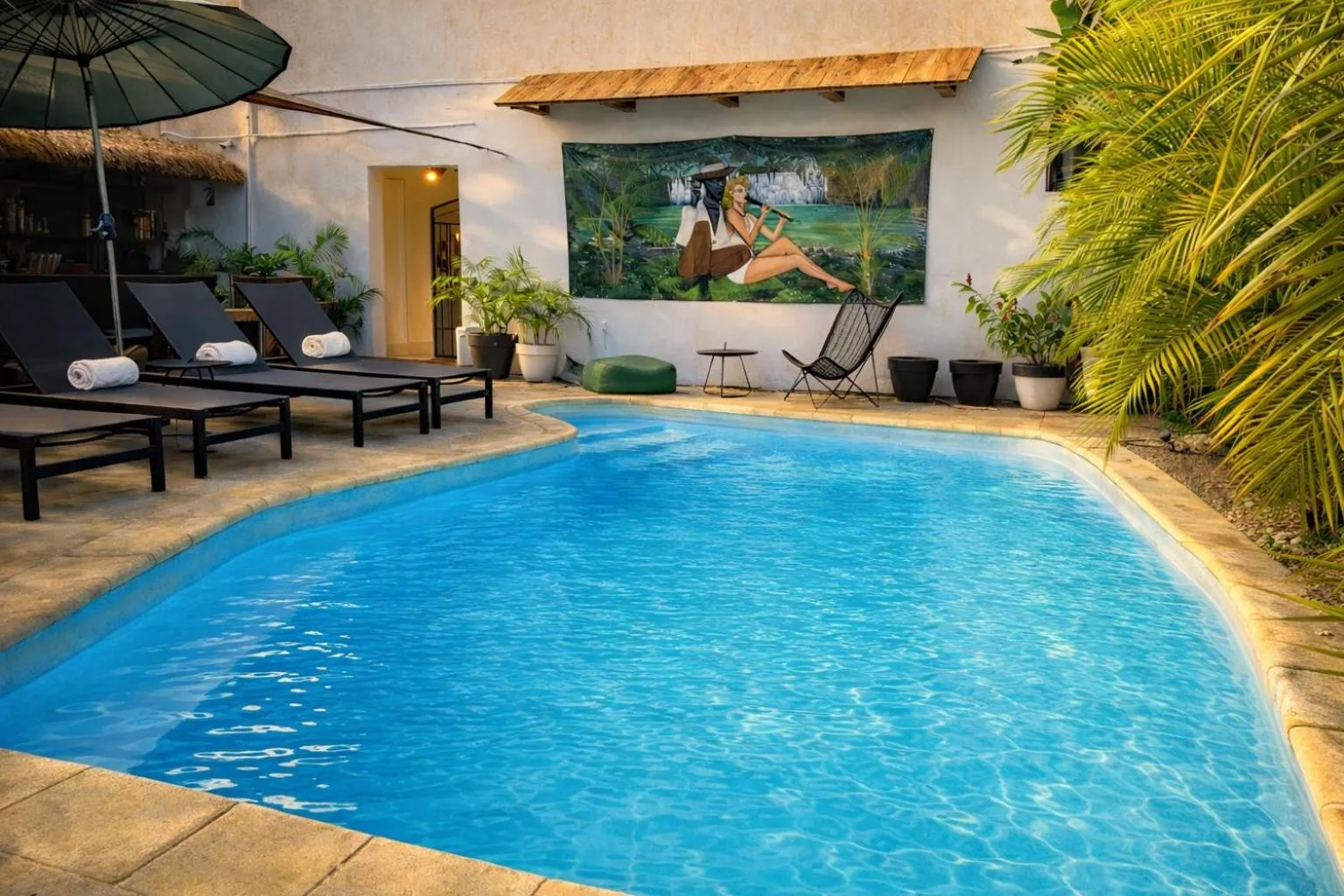 Transats bleus alignés au bord d'une piscine turquoise dans un jardin tropical.