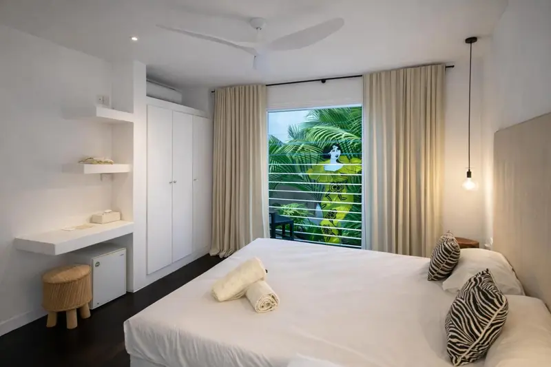 Une chambre lumineuse avec un grand lit et une vue sur la végétation luxuriante.