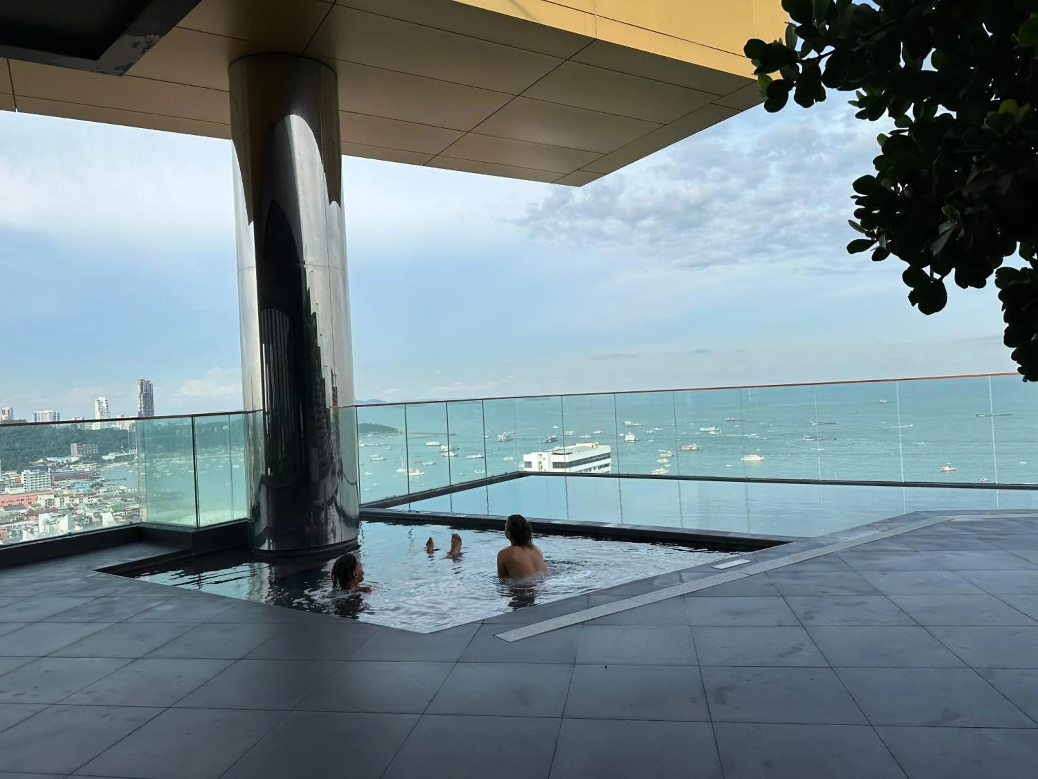 Baigneurs dans une piscine à débordement avec vue sur la mer et la ville.