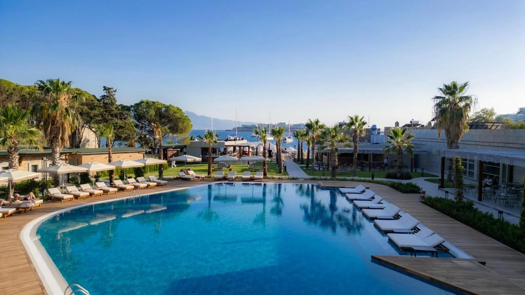 Une piscine turquoise bordée de transats, avec une végétation luxuriante et une vue sur la mer.