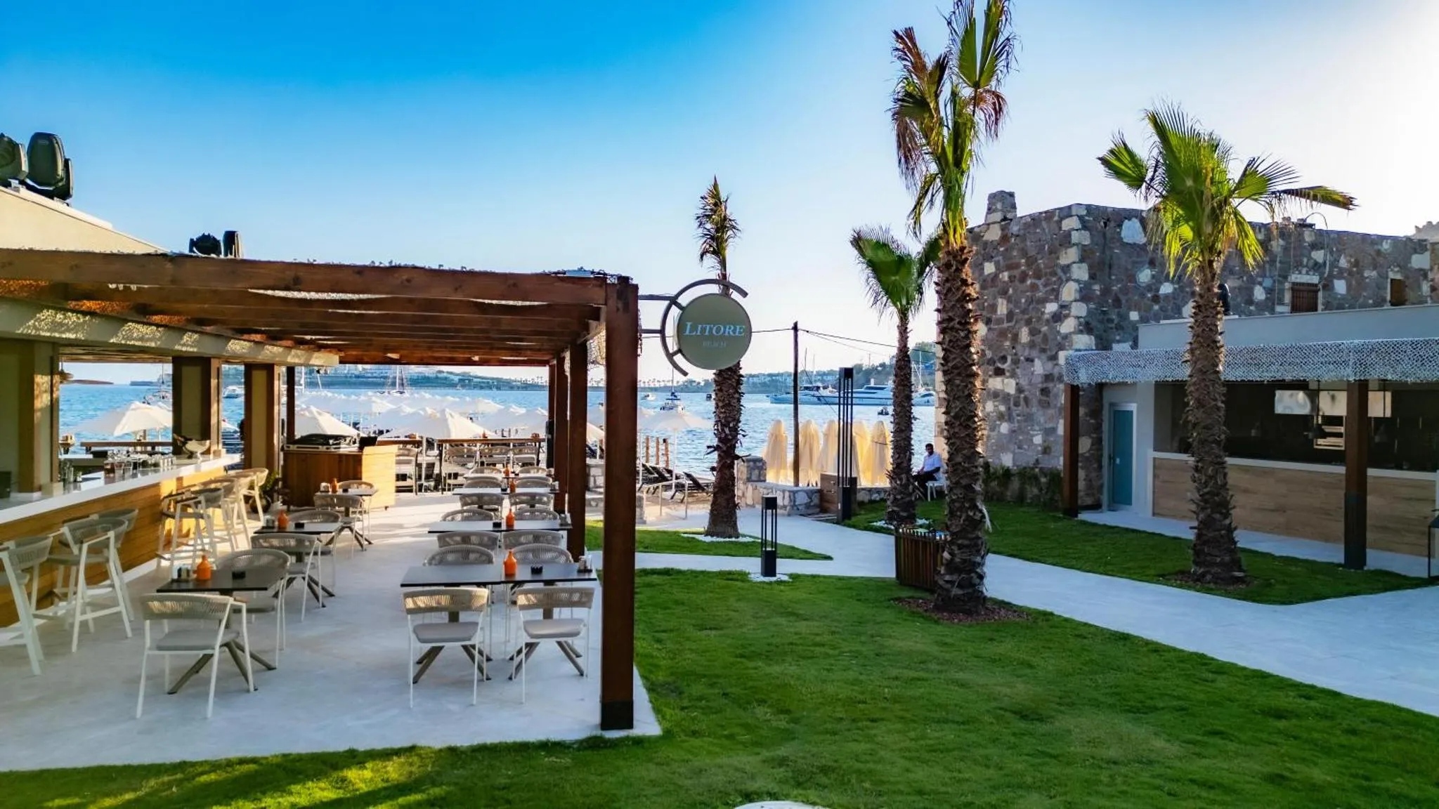 Terrasse ombragée avec tables et chaises donnant sur la mer.