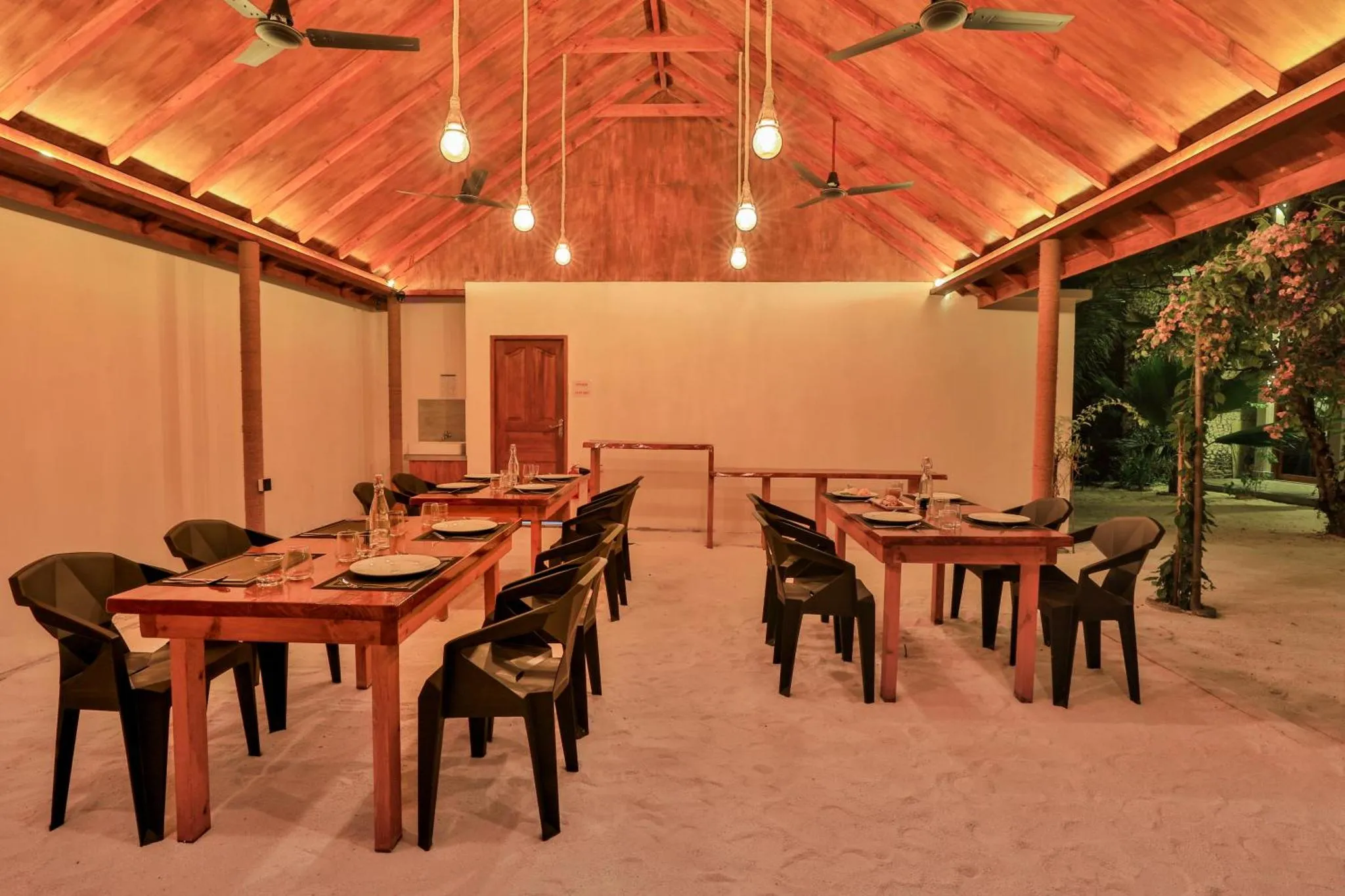 Une salle à manger extérieure avec des tables dressées et un éclairage chaleureux.