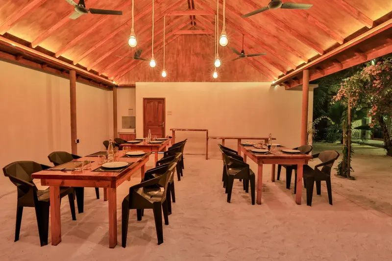 Une salle à manger extérieure avec des tables dressées et un éclairage chaleureux.
