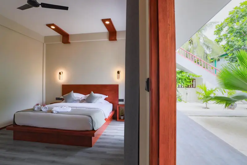 Une chambre lumineuse avec un grand lit et une ouverture sur une cour verdoyante.