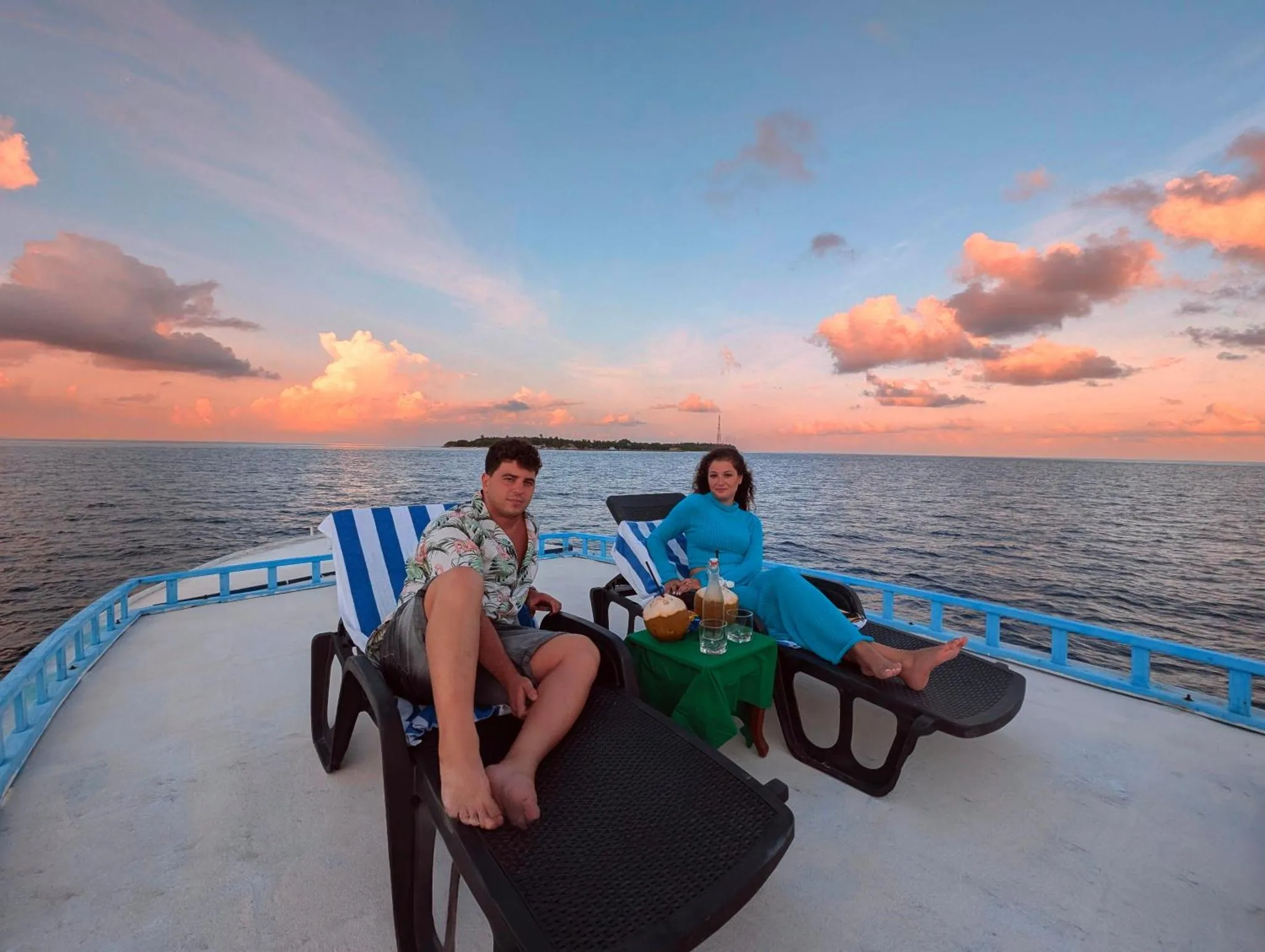 Un couple se détend sur des chaises longues à bord d'un bateau au coucher du soleil.