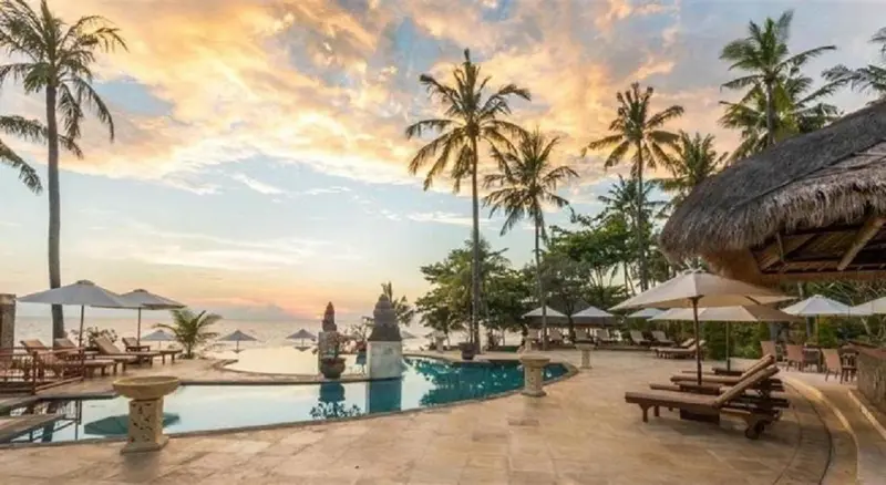 Une piscine bordée de transats et de palmiers au coucher du soleil.