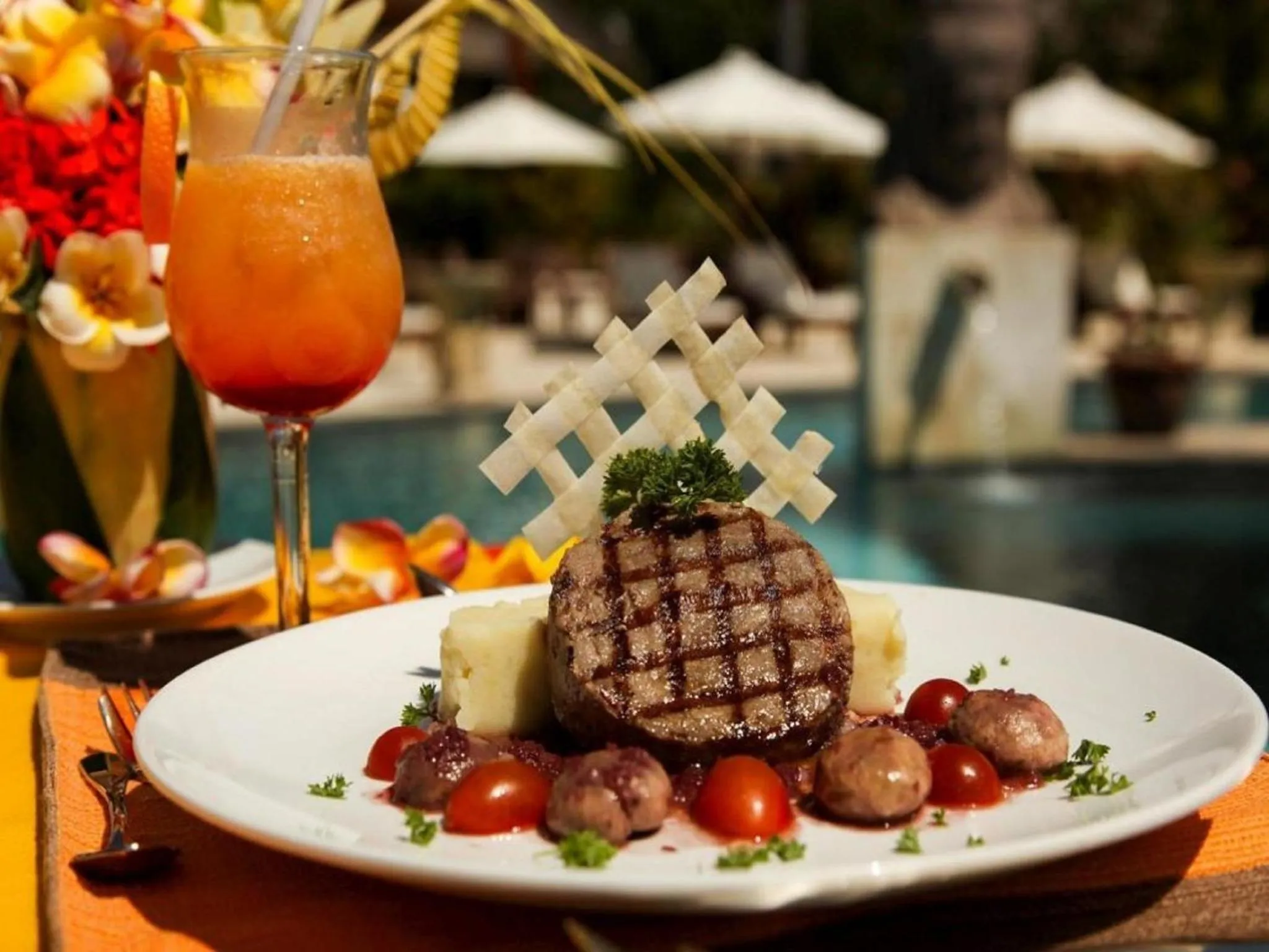 Assiette de viande grillée accompagnée d'une boisson orangée et de quelques légumes.