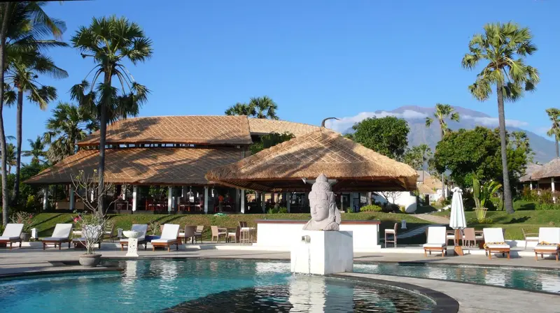 Une piscine turquoise bordée de chaises longues devant un bâtiment à toit de chaume.