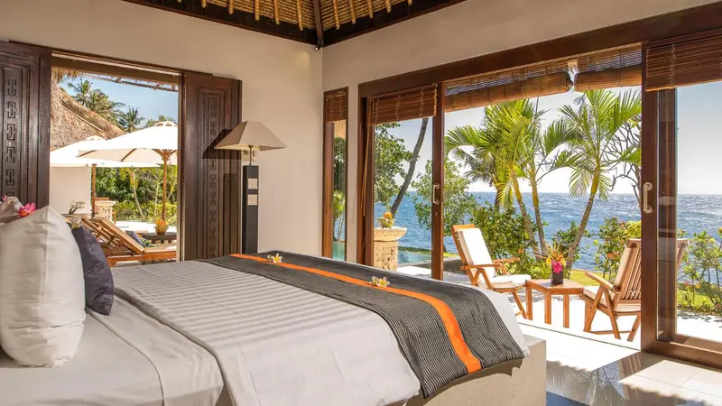 Une chambre lumineuse s'ouvre sur une vue sur la mer et une végétation tropicale.