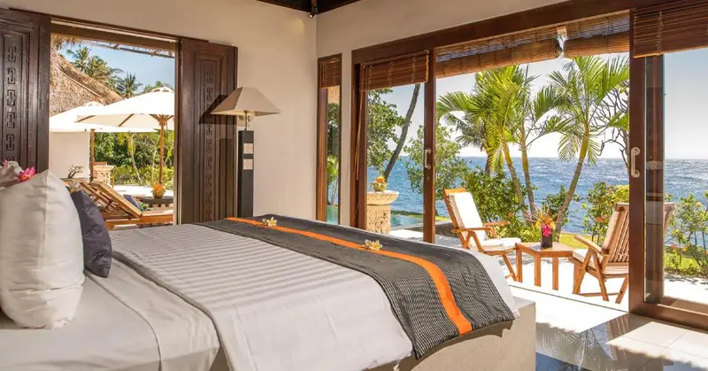 Une chambre lumineuse s'ouvre sur une vue sur la mer et la végétation tropicale.
