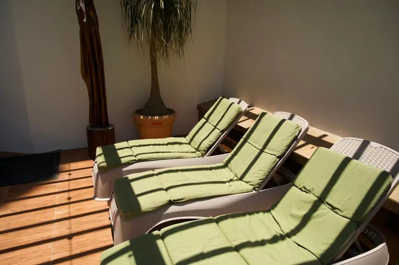 Transats verts et blancs sur une terrasse en bois baignée de soleil.