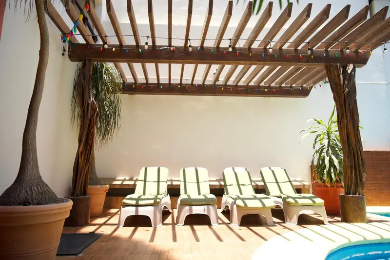 Transats blancs disposés sous une pergola en bois et plantes vertes.