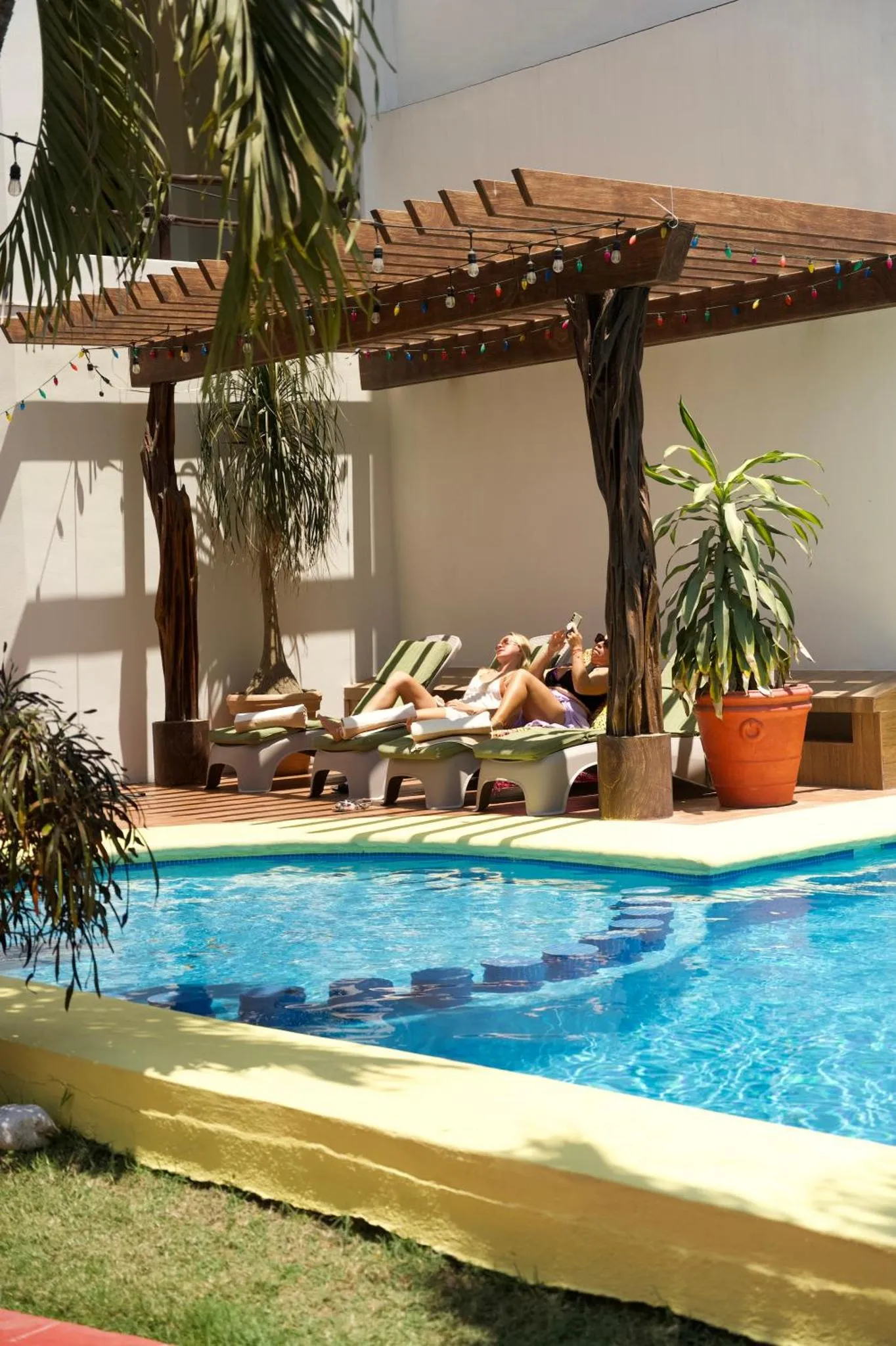 Espace de détente avec piscine et chaises longues à l'ombre d'une pergola.