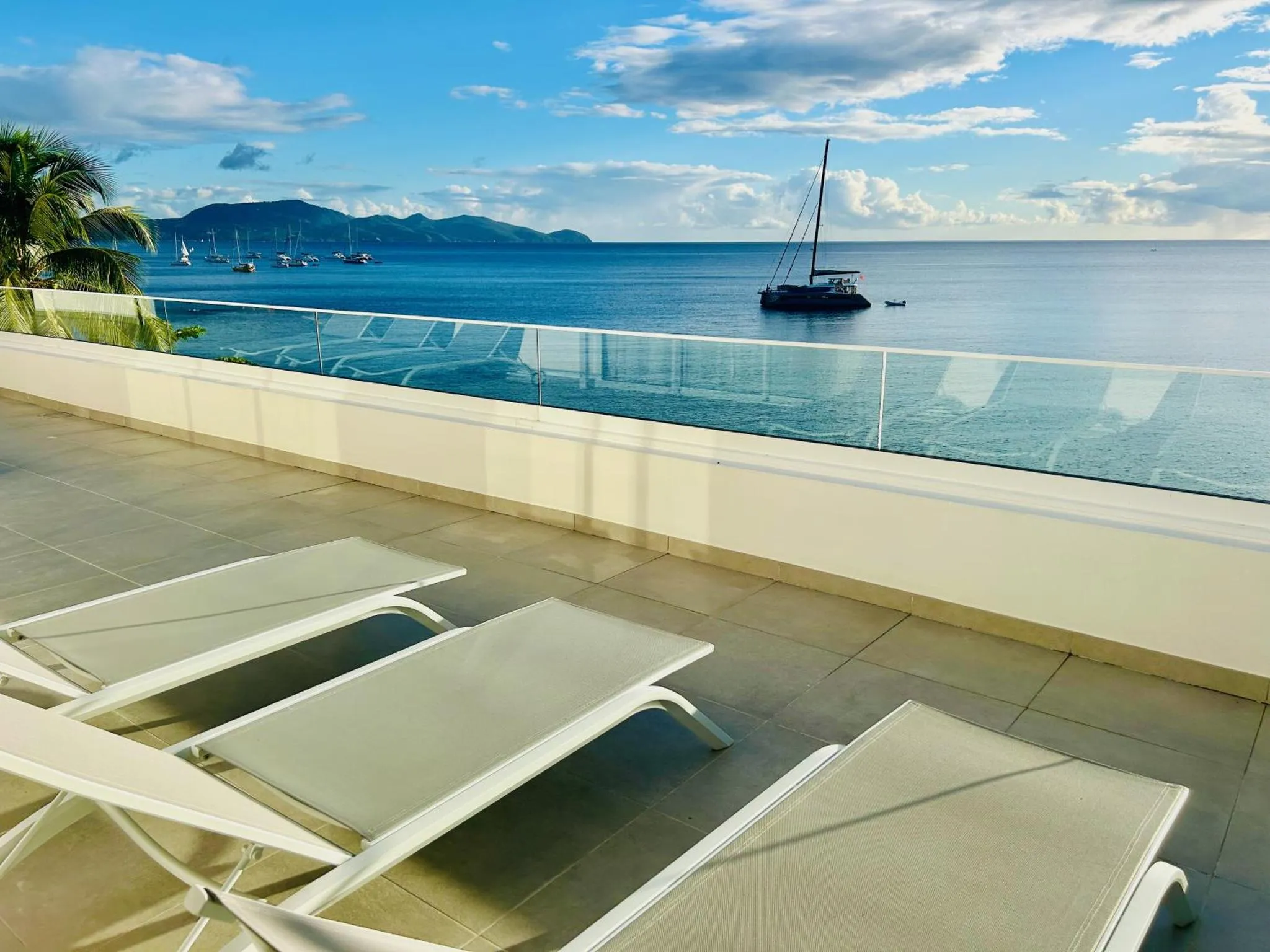 Terrasse ensoleillée avec transats et vue sur la mer et les bateaux.