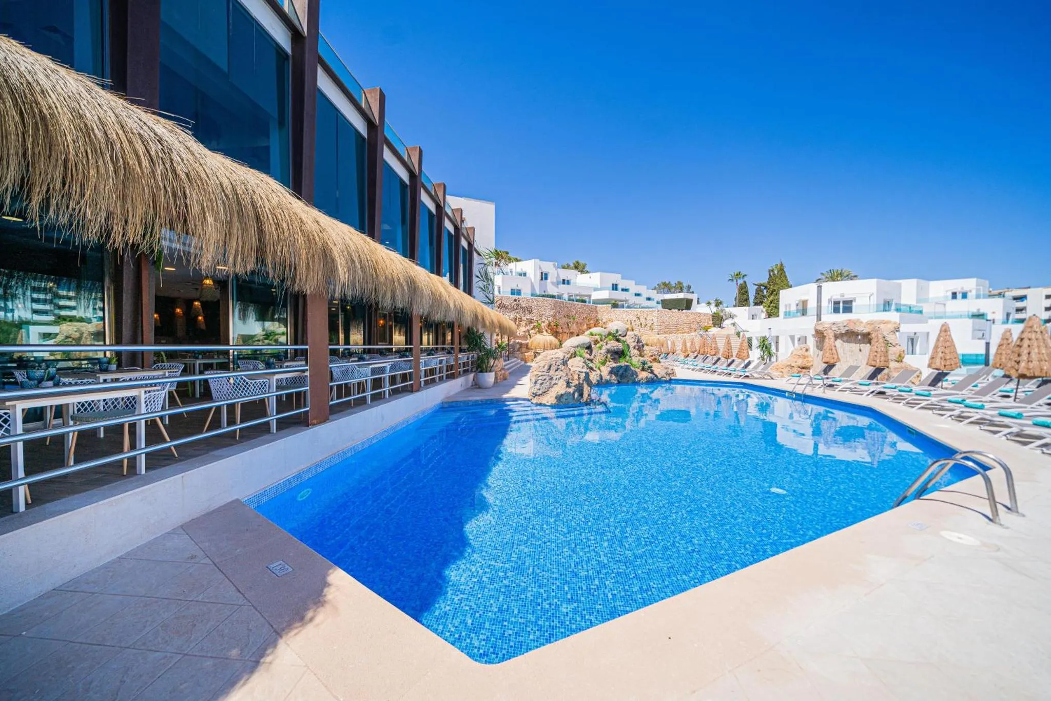 Une piscine rectangulaire avec des transats et des parasols, bordée d'une terrasse ombragée.