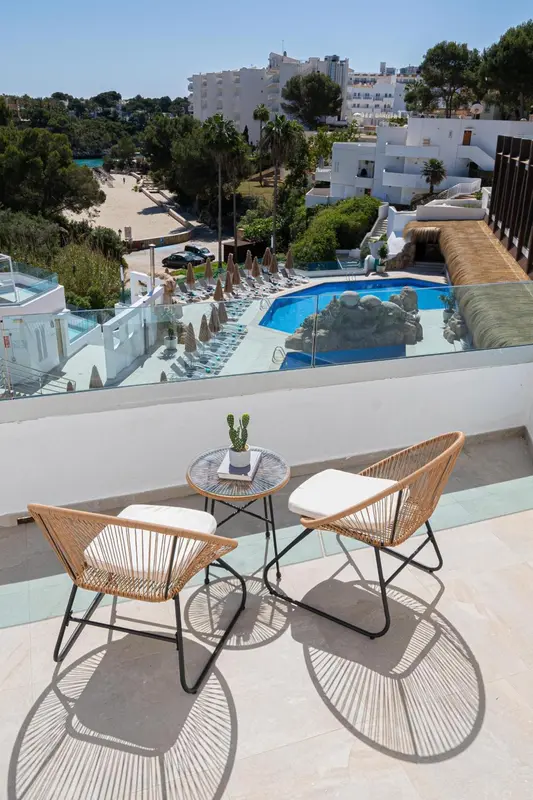 Terrasse avec mobilier en osier et vue sur une piscine et la mer.