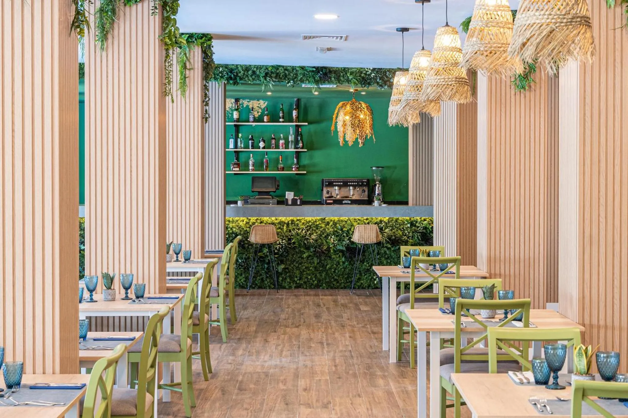 Une salle de restaurant lumineuse avec des tables vertes et des suspensions en fibres naturelles.