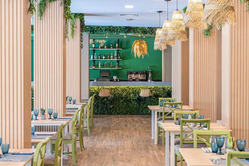 Une salle de restaurant lumineuse avec des tables vertes et des suspensions en fibres naturelles.