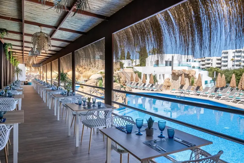 Une salle à manger lumineuse avec des tables dressées face à une piscine et à la mer.