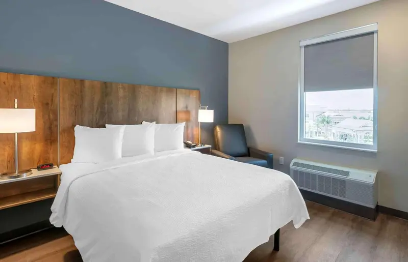 Une chambre lumineuse avec un grand lit et un fauteuil près de la fenêtre.