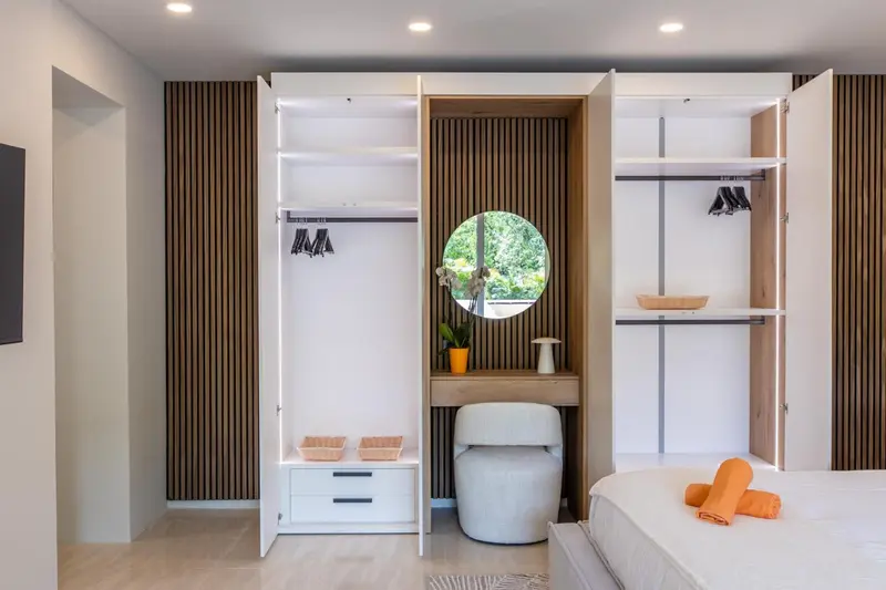 Une armoire ouverte révèle un espace de rangement et un coin bureau avec un miroir rond.