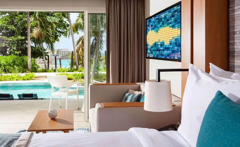 Une chambre lumineuse s'ouvre sur une vue verdoyante et une piscine.