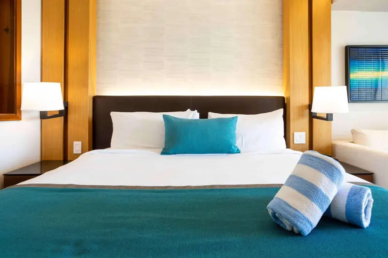 Une chambre lumineuse avec un grand lit recouvert d'une courtepointe turquoise et de coussins.