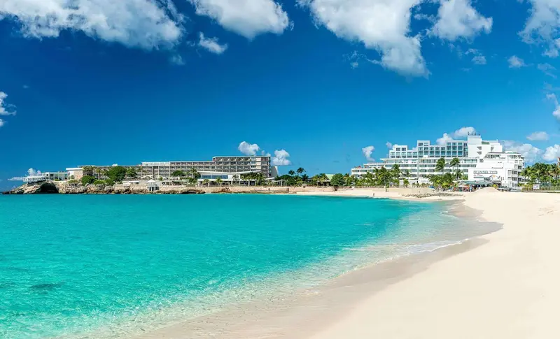 Vue aérienne d'une plage de sable blanc bordée d'eaux turquoise et d'hôtels.