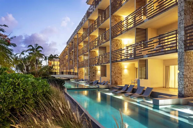 Bâtiment moderne avec des balcons donnant sur une piscine et une végétation luxuriante.