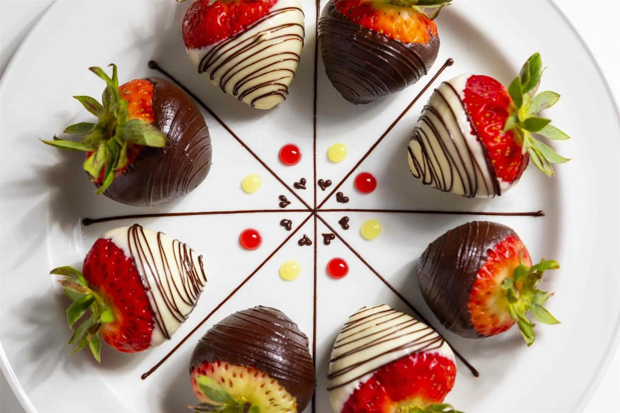 Fraises enrobées de chocolat disposées en cercle sur une assiette blanche.