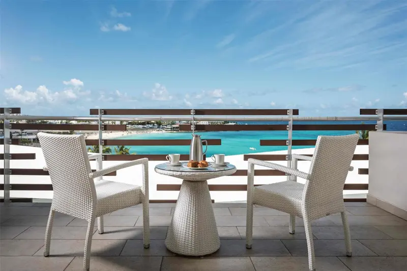 Deux fauteuils et une table basse avec un petit-déjeuner surplombent une plage turquoise.
