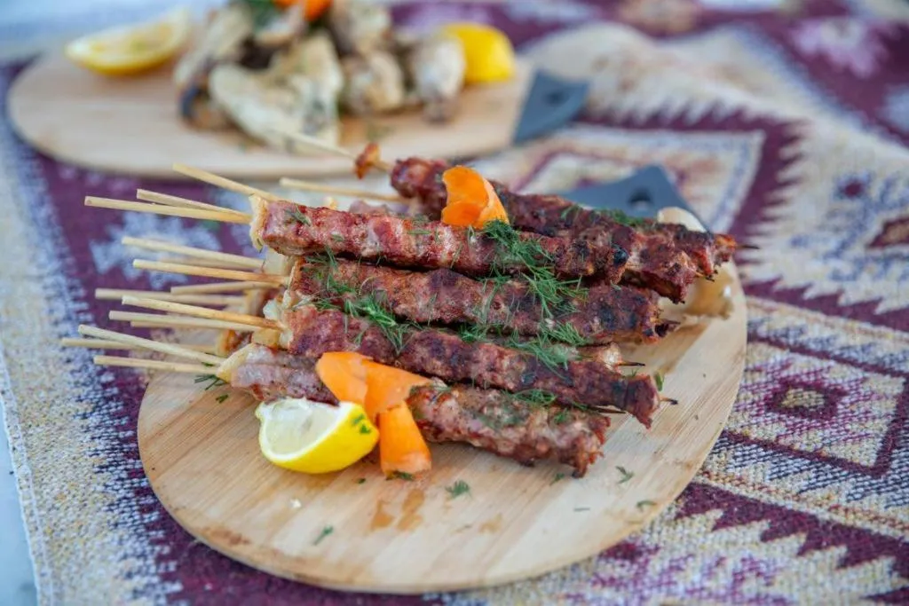 Assiette de brochettes de viande grillée, garnies de légumes et de citron.