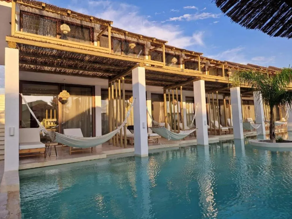 Terrasse ombragée avec des hamacs au-dessus d'une piscine turquoise.