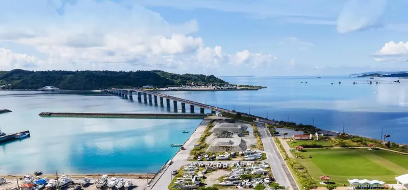 Vue aérienne d'une route sur pilotis reliant deux îles verdoyantes au-dessus d'une eau turquoise.