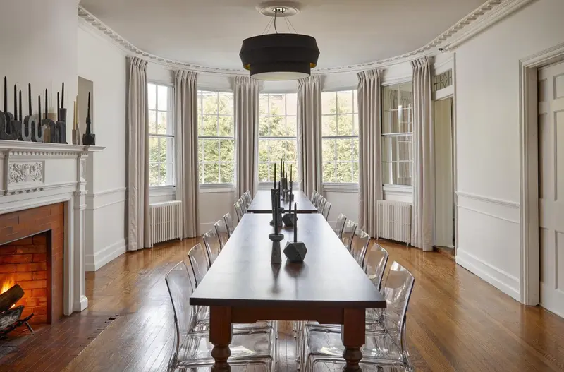 Une longue table en bois est mise en scène dans une pièce lumineuse avec une cheminée.