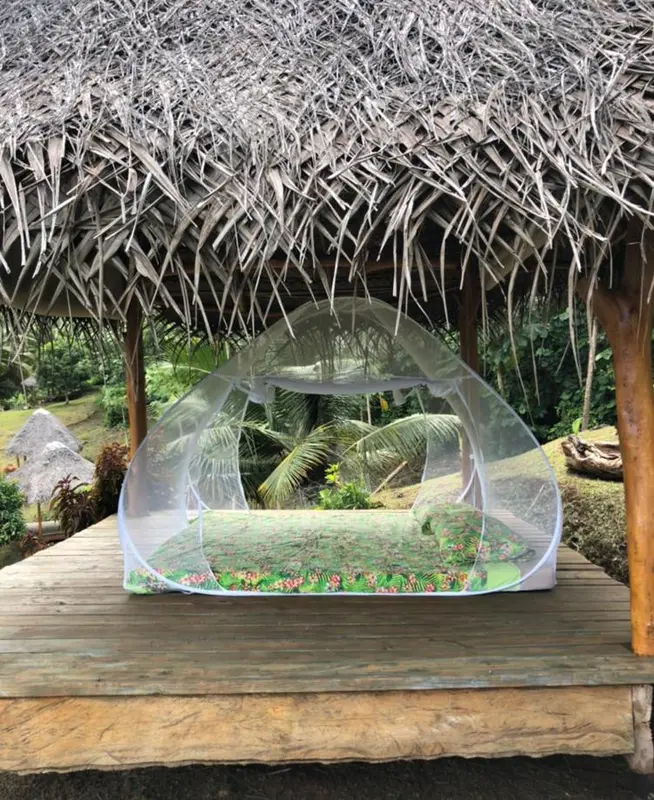 Un lit recouvert d'une moustiquaire se trouve sur une terrasse en bois couverte de chaume.