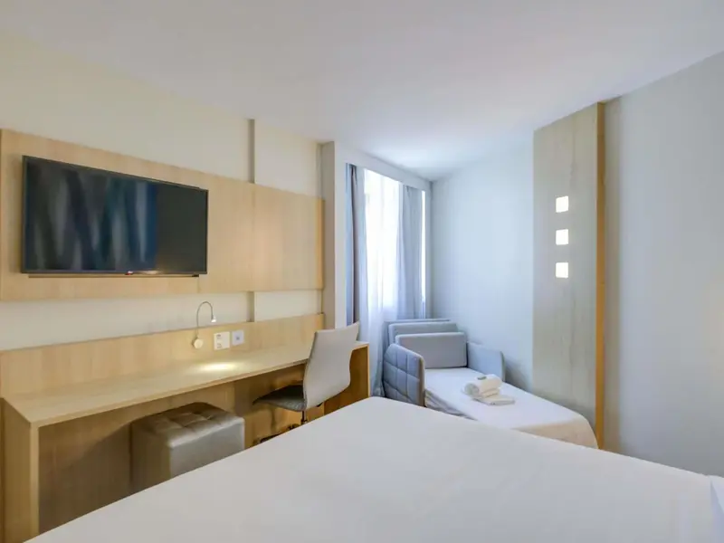 Une chambre lumineuse avec un lit, un bureau et un canapé près d'une fenêtre.