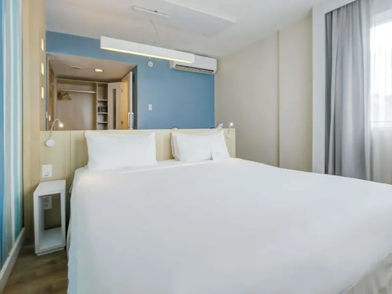 Une chambre lumineuse avec un grand lit recouvert d'une couette blanche.