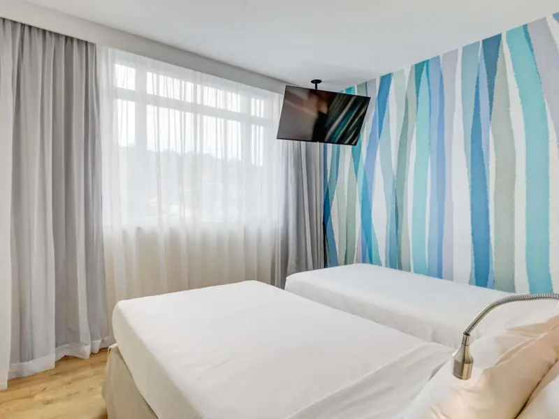 Une chambre lumineuse avec deux lits simples et un mur décoratif.