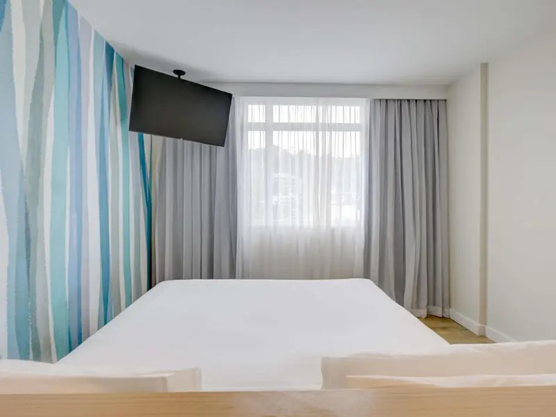 Une chambre lumineuse avec un lit blanc et un mur décoré de motifs ondulés.