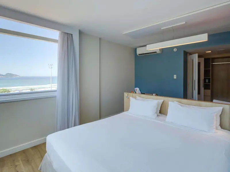 Chambre lumineuse avec un grand lit blanc et vue sur la mer.