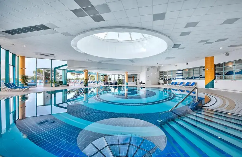 Une piscine intérieure aux formes géométriques et aux couleurs vives, baignée de lumière naturelle.