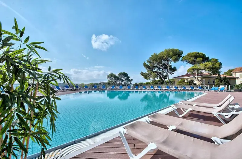Une piscine rectangulaire bordée de transats sous un ciel bleu.