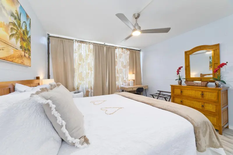 Une chambre lumineuse avec un grand lit recouvert d'une courtepointe blanche et de coussins.