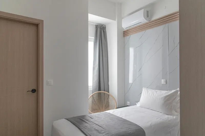 Une chambre lumineuse avec un lit simple et un fauteuil en rotin.