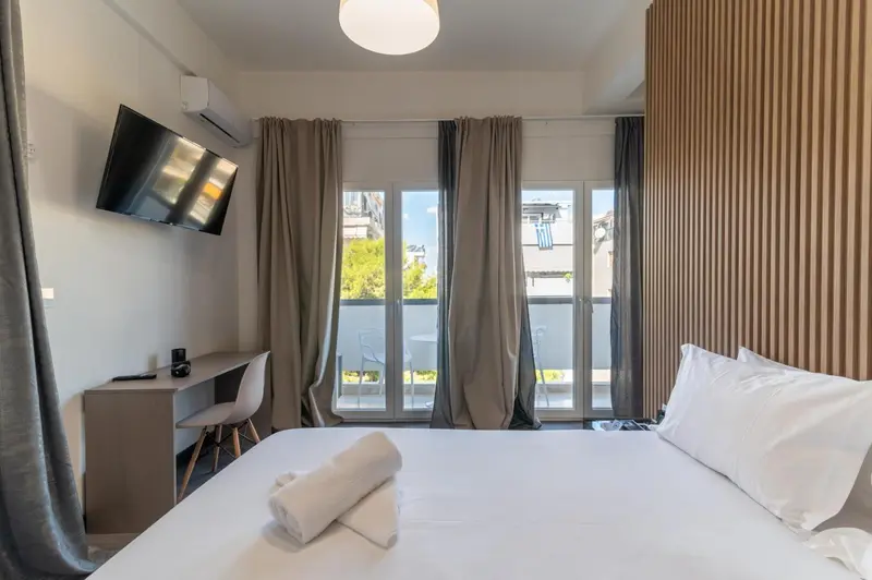 Une chambre lumineuse avec un lit fait et un bureau près d'une baie vitrée.