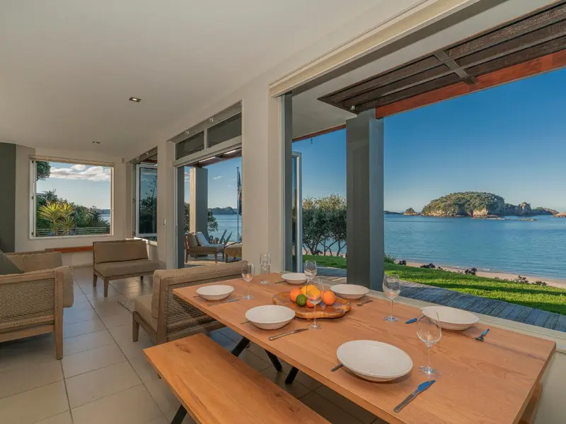 Une table est dressée dans une salle à manger ouverte sur une terrasse et une vue sur la mer.