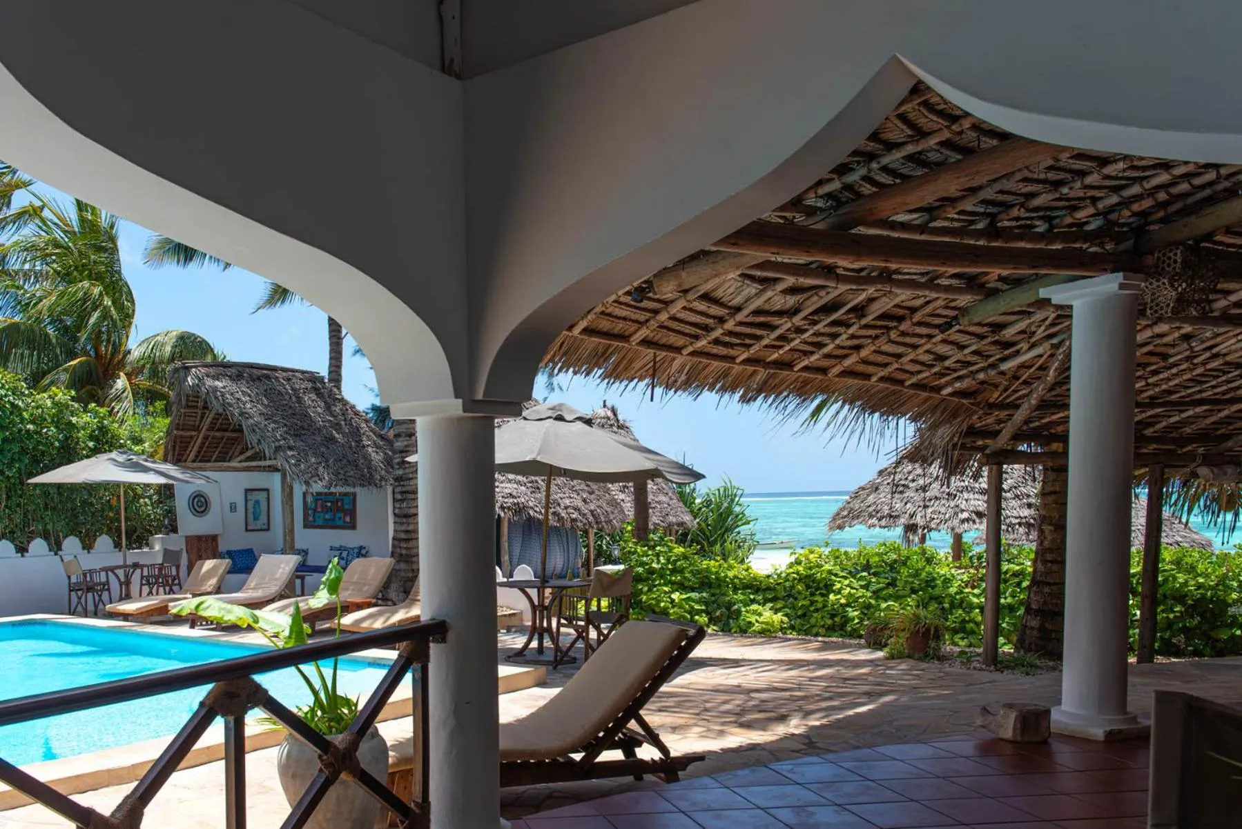 Espace de détente ombragé avec transats et piscine turquoise en bord de mer.